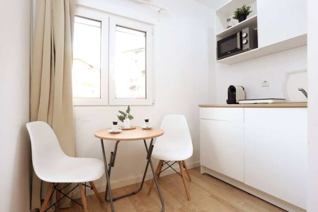 Estúdio T0: kitchenette com micro-ondas, máquina de café, placa e lava-loiça, mesa redonda e duas cadeiras brancas