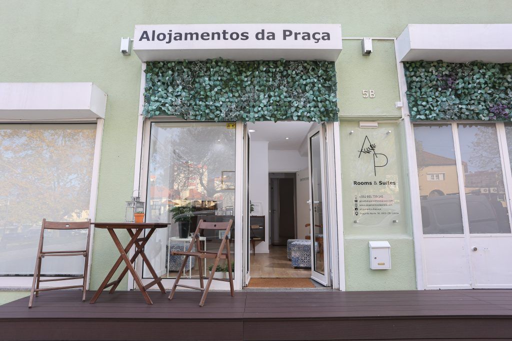 Fachada verde do Alojamentos da Praça, na Praça do Norte 5B, com o letreiro, jardim vertical e esplanada