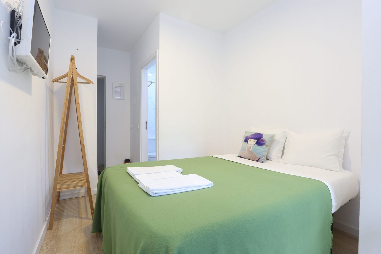 Quarto 3: cama de casal com manta verde, televisão na parede e porta para a casa de banho