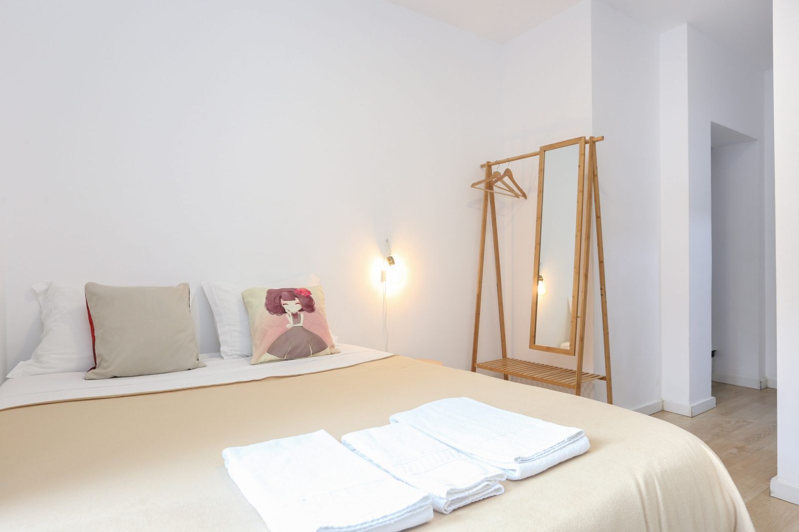Suite 1: cama de casal com colcha bege, toalhas dobradas e cabide de bambu com espelho